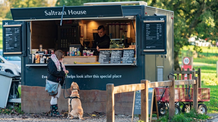 A woman with her dog pays for a coffee at the kiosk in the grounds of Saltram